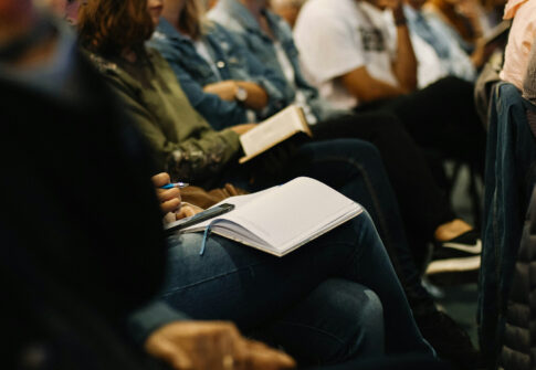 Gruppo di studenti in ascolto, che prendono appunti su bloc notes e smartphone