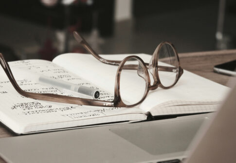 scrivania con notebook, ed un paio di occhiali accanto ad un quaderno con appunti